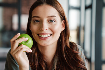 Beautiful happy nice woman smiling at camera while eating apple