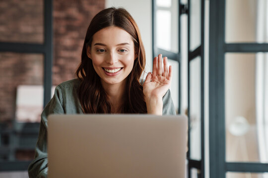Beautiful smiling woman waving hand and working with laptop