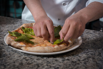 Obraz na płótnie Canvas hands of the chef decorating handmade pizza with basil leaves