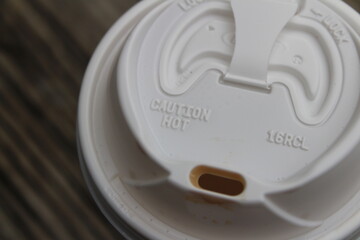 The lid from a plastic coffee cup to go against a wooden background.