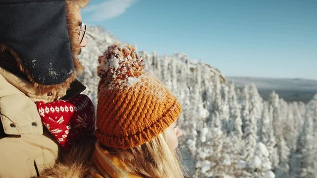 Young romantic couple in outerwear enjoying beautiful view from mountain peak and taking picture of nature with smartphone while hiking in national park on winter day