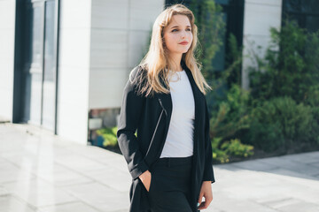 Plakat a cute blonde in a business black suit walks around the territory of a business center 