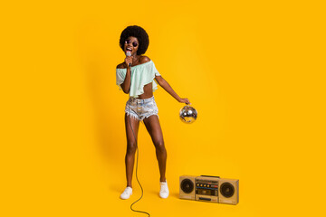 Full length body size photo of black skinned girl performing song with disco ball at concert with...
