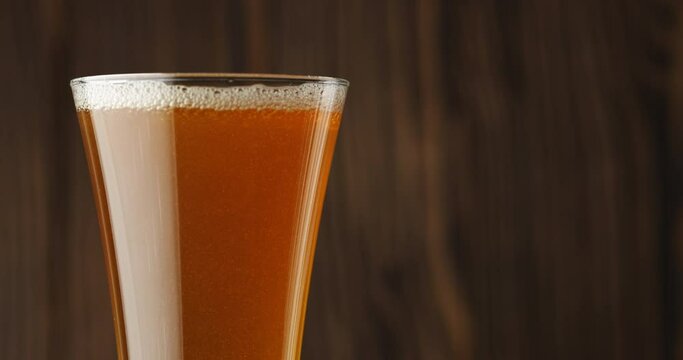 Cold beer is slowly poured into a glass on a dark wooden background, there is a lot of foam and bubbles in the glass. Slow motion. Beer is pouring into a glass isolated on a wooden background. 
