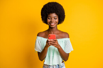 Photo portrait of girl holding phone in two hands texting isolated on vivid yellow colored background