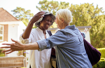 Happy senior women friends greeting and hugging in sunny garden