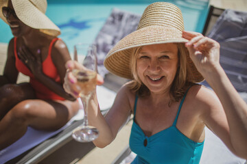 Portrait happy senior woman drinking champagne at sunny poolside