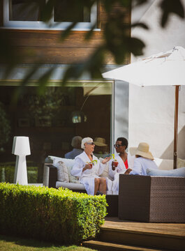 Senior women friends relaxing in spa robes on sunny hotel patio