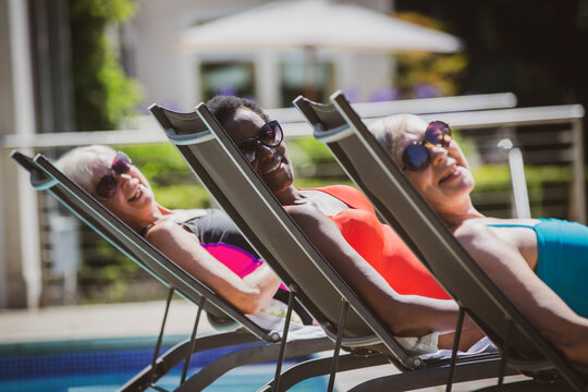 Portrait carefree senior women friends sunbathing at sunny poolside
