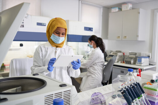 Female scientist in face mask and hijab using digital tablet in laboratory