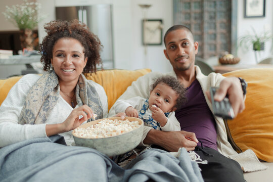 Happy couple with baby daughter watching TV and eating popcorn
