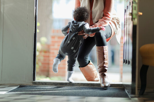 Mother lifting baby daughter in pajamas at front door