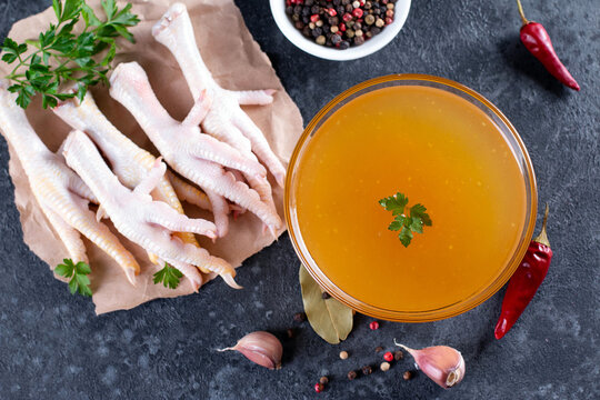 Chicken bone broth in glass plate, with fresh vegetables, spices and herbs on gray background. Top view