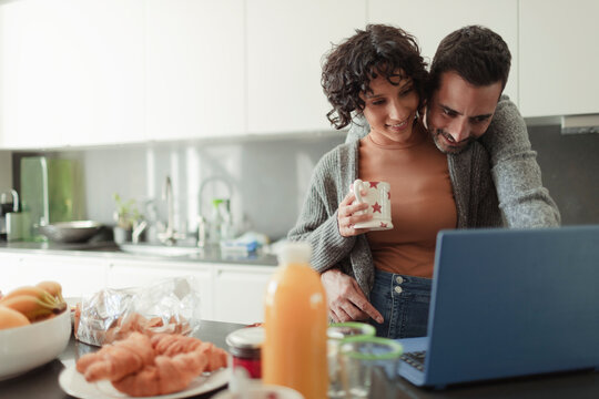 Affectionate couple working at laptop in morning kitchen