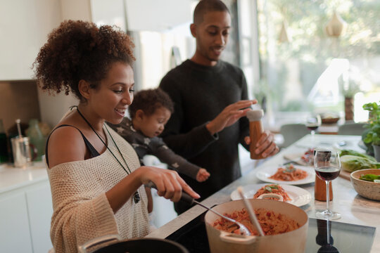 Couple with baby daughter cooking pasta at kitchen stove