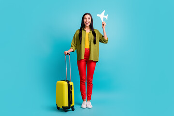 Full length photo of girl hold big case paper plane open mouth wear green shirt pants sneakers isolated blue color background