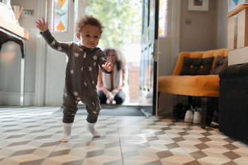 Cute baby girl in star pajamas learning to walk at home