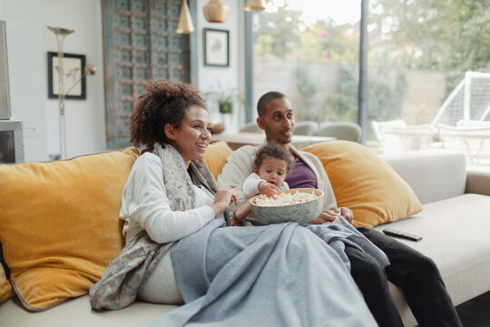 Parents with baby daughter watching movie with popcorn on sofa