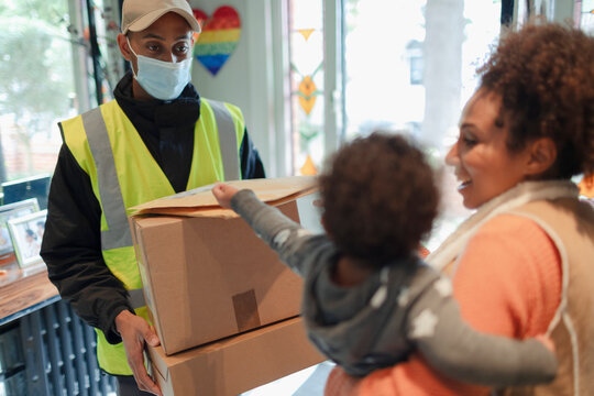 Mother and baby daughter receiving packages from delivery man in mask