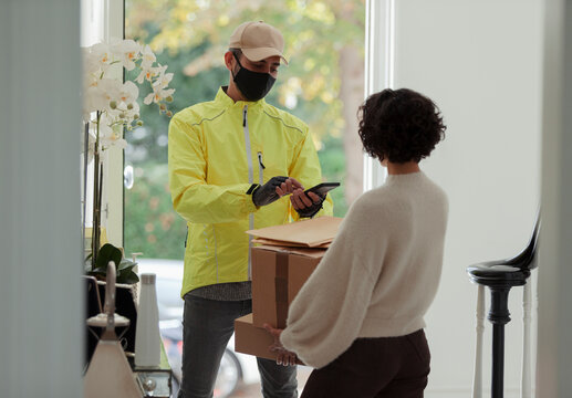Woman receiving package from delivery man in face mask at front door