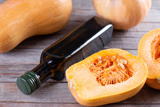 Pumpkin seed oil in a glass jar and fresh raw pampkin on wooden table. Healthy eating, diet or vegan food concept.