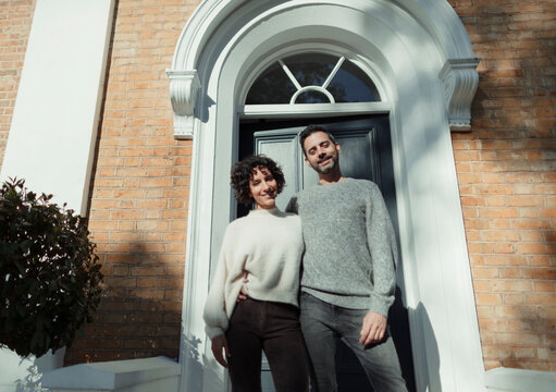 Portrait happy couple standing at front door on sunny house stoop