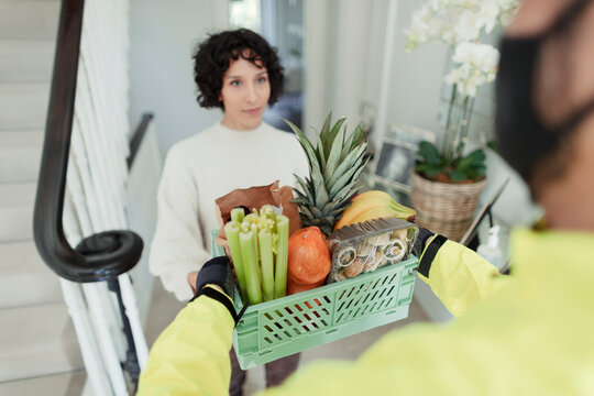 Woman receiving grocery delivery from courier in face mask