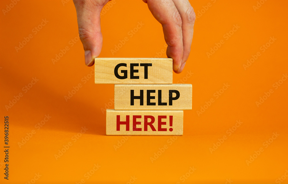 Wall mural get help here symbol. male hand builds stack from blocks with words 'get help here'. beautiful orang
