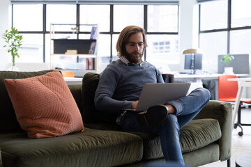 Obraz premium Caucasian businessman using laptop sitting on sofa in creative office