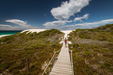 Fototapeta na wymiar Woman walking along wooden footpath leading to sand dunes at De Hoop nature Reserve, South Africa.