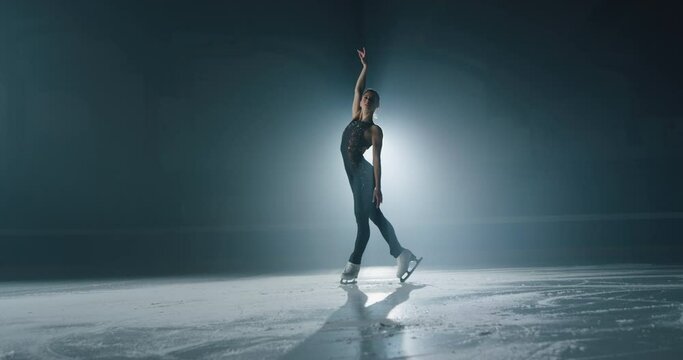 Cinematic shot of young female artistic figure skater is performing a woman's single skating choreography on ice rink before start of a competition. Concept of perfection, precision, freedom, passion.
