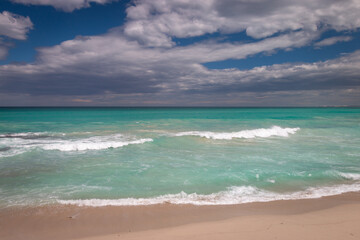 Beach with turquoise colored water against blue sky with clouds.