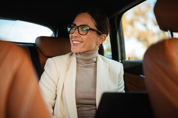 Beautiful smiling businesswoman working with laptop while sitting in car