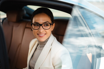 Beautiful happy businesswoman in eyeglasses smiling while sitting in car