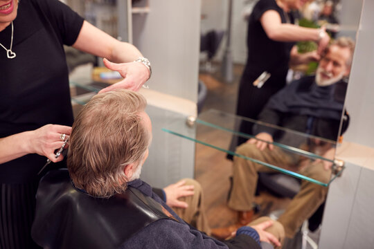 Senior Man Having Hair Cut By Female Stylist In Hairdressing Salon