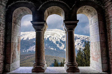 Beautiful gothic medieval arched stone window. Magnificent majestic view from the window. Winter mountains and a castle