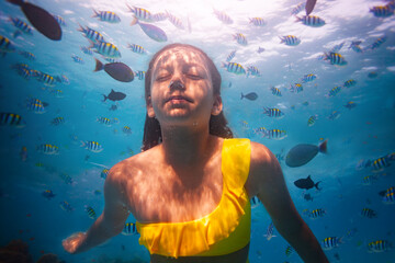 Underwater portrait of a girl diving among fish with her eyes closed