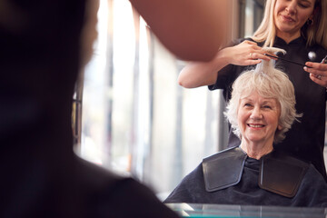 Senior Woman Having Hair Cut By Female Stylist In Hairdressing Salon