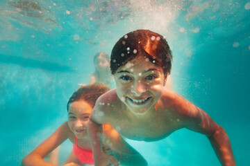 Underwater portrait of the smiling boy in the bool with friends girls on background