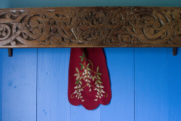 folklore embroidery of Iceland with flowers on dark red cloth hanging off carved wooden lintel against a blue painted background 