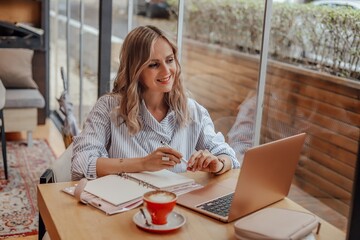 Woman working on a notebook in a cafe. Next to it is a cup of coffee and a diary.