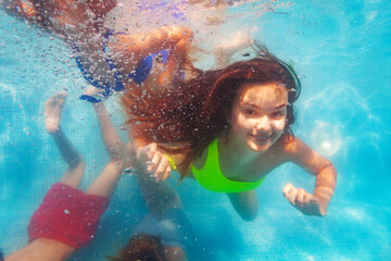 Smiling girl with long hair in group of three friends children dive underwater together