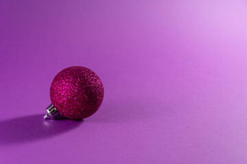 Pink christmas ball on a purple background, christmas time, copy space.