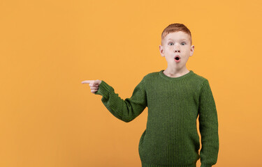 Excited ginger boy in green sweater pointing at copy space