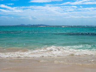 A tropical seascape with white water breaking on sand beach and turquoise sea and distant Caribbean Island in distance