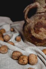 Vintage clay pot on black background and linen texture with walnuts. Close up