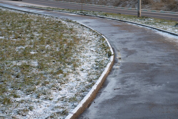 Pedestrian sidewalk, curb and lawn lightly powdered with snow, background