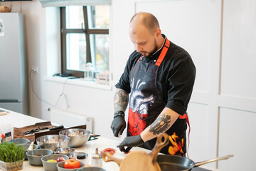 A tattooed chef in black gloves carves meat. Cutting minced meat with a knife in a modern kitchen.