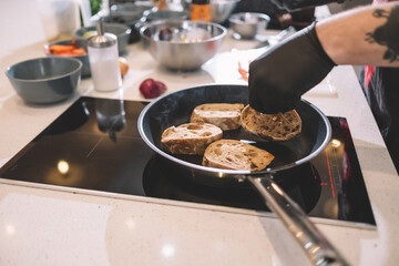 The cook in black rubber gloves removes the croutons from the pan.