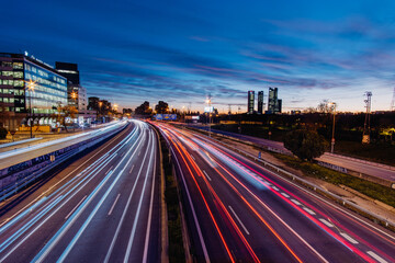 Fototapeta na wymiar Highway A-1in Madrid Spain with car light trails at rush hour at sunset with Cuatro Torres Business area in the background